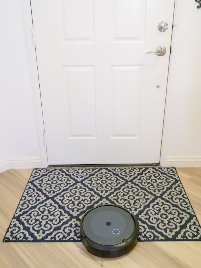 A modern robotic vacuum cleaner operating on a patterned rug near a white door.
